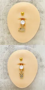 Detalle de piercing de ombligo de acero dorado con dijes de elefante y buho de circonita.