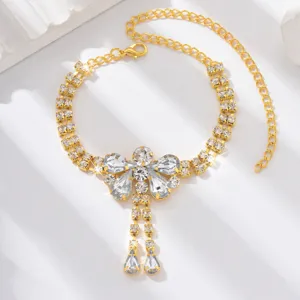 Gold rhinestone anklet close-up, sparkling crystal butterfly pendant detail on white background.