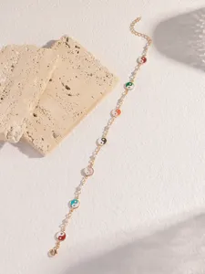 Nahaufnahme des goldenen Kettenarmbands mit bunten emaillierten Yin-Yang Symbolen und Perlen.