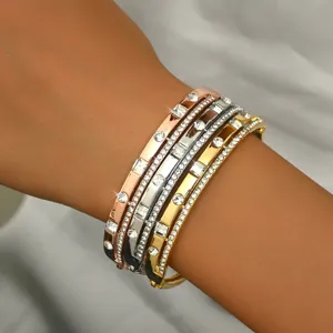 Primo piano di bracciali rigidi geometrici impilati con strass in oro, argento e oro rosa.