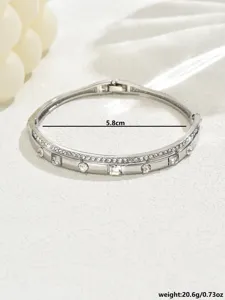 Bracciale rigido geometrico in metallo argentato con cristalli trasparenti, vista dettagliata.