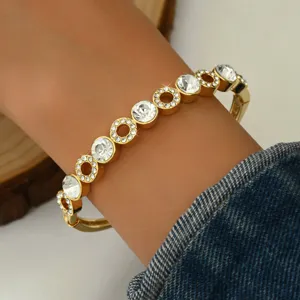 Primo piano dettagliato di un bracciale geometrico dorato con strass indossato al polso.
