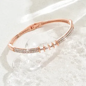 Primo piano dettagliato di un bracciale rigido geometrico in oro rosa con strass luminosi.