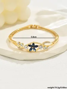 Close-up of gold-tone hinged bangle bracelet with dark blue floral center and clear crystals.