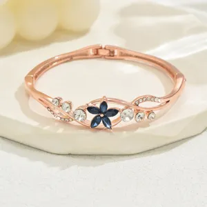 Close-up detail of rose gold hinged rhinestone flower bracelet, sparkling blue crystal centerpiece.