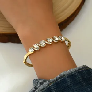 Primo piano di un bracciale rigido dorato con cerniera, decorato con pietre di cristallo.