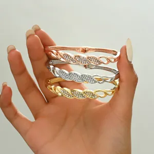 Primo piano dettagliato di tre bracciali rigidi geometrici con strass in oro, argento e oro rosa.