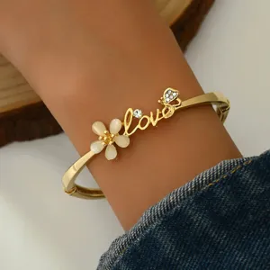 Close-up detail of a gold-tone floral Love bangle bracelet worn on wrist with denim sleeve.