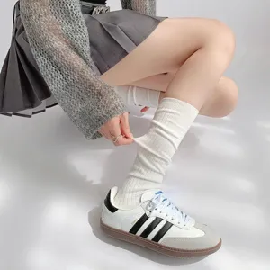 Detailopname van witte slouch sokken gecombineerd met geplooide rok en sneakers, collegestijl.