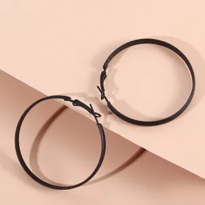 Gros plan sur de grandes boucles d'oreilles créoles noires mates, design moderne et élégant.
