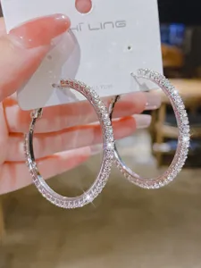 Boucles d'oreilles créoles grandes strass argentées scintillantes sur carte, bijoux de mode chic.