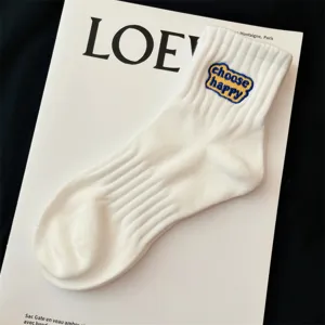 White ribbed mid-tube socks featuring a cute embroidered choose happy patch detail close up.