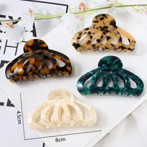 Vue détaillée de grandes pinces à cheveux en acrylique avec motif floral évidé et écaille.