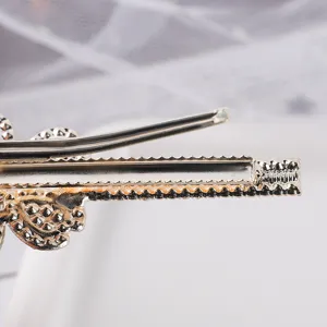Metal duckbill hair clip close-up, elegant metallic finish with delicate textured edge detail.