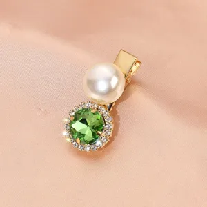 Detail shot of a vintage green rhinestone hair clip featuring a large pearl and shiny crystals.