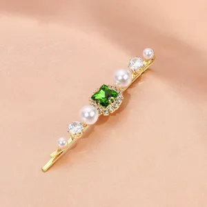 Detail view of a gold rhinestone pearl hair clip with a vintage square green zircon stone.