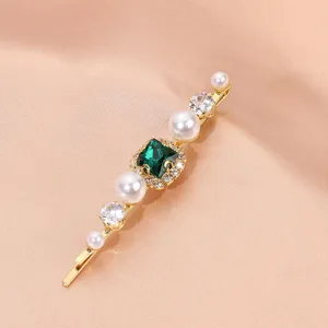 Close-up detail shot of the golden hair clip featuring sparkling green square zircon and pearls.