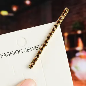 Rhinestone hair clip detail view, gold metal bobby pin with amber crystals on card display.