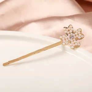 Gros plan détail d'une épingle à cheveux dorée avec motif trèfle perlé et strass.