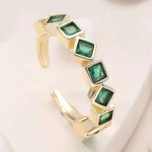 Gros plan sur la bague ouverte dorée ornée de pierres de zircone vert carré étincelantes.