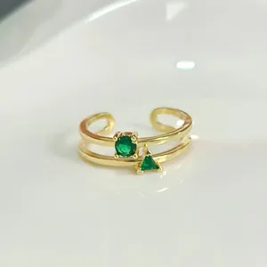 Gros plan sur une bague double en or avec des oxydes de zirconium verts ronds et triangles.