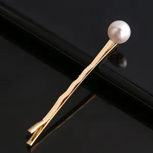 Détail de pince à cheveux en métal doré, élégante épingle avec perle pour coiffure.