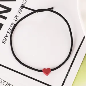Primer plano detallado de una goma de pelo elástica negra con un colgante de corazón rojo mate.