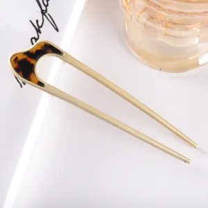 Detail shot of a minimalist U-shaped hair fork with matte metal and stylish acetate top.