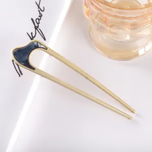 Detail view of a modern minimalist U-shaped hair fork in matte gold metal with chic dark accent.