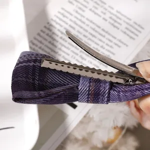 Close-up detail of a purple plaid fabric bow hair clip with metal alligator clip, elegant style.