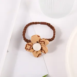 Gros plan d'un élastique à cheveux tressé marron avec fleur en tissu et cœur blanc.