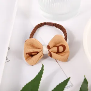 Vue détaillée de l'élastique à cheveux en tissu avec nœud et bande tressée marron chic.