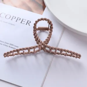 Close-up detail shot of matte brown metal hair claw clip with unique twist design texture.