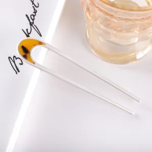 Detail view of a minimalist U-shaped hair fork with frosted metal and amber acetate accent.