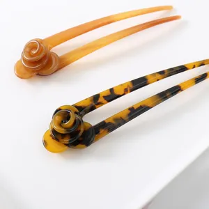 Close-up detail of elegant acetate U-shaped hair pins featuring stylish floral designs in amber.