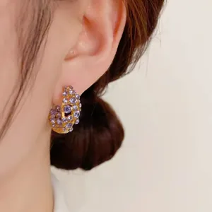 Close-up detail shot of sparkling purple rhinestone paved gold hoop earrings worn on ear.