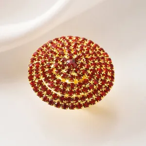 Dettaglio in primo piano del grande anello cocktail con strass rossi e base dorata lucida.