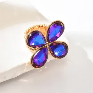 Primo piano di un elegante anello in strass regolabile con cristalli blu viola e base dorata.
