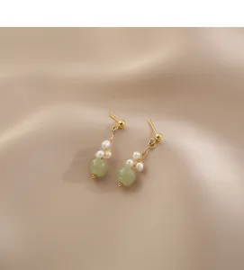 Detailed close-up of dainty gold-toned dangle earrings with green jade beads and pearls.