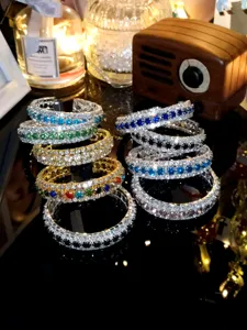 Nahaufnahme glitzernder dreireihiger Strass-Armreifen auf dunklem, reflektierendem Tisch.