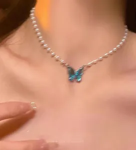 Close-up detail shot of the elegant pearl choker necklace featuring a sparkling blue crystal butterfly pendant.