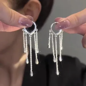 Close-up detail showing exquisite silver heart and tassel earrings held in hand for display.