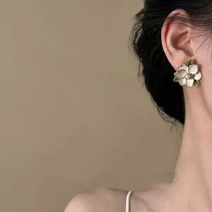 Close-up of a delicate white flower stud earring with green leaves and a pearl center.