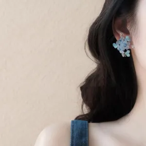 Dettaglio primo piano orecchini a lobo fiori perline blu, stile gioiello dolce fresco.