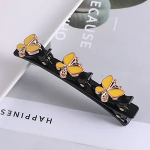 Detailopname van zwarte dubbellaagse haarspeld met gele vlinders en strass-steentjes voor haar.