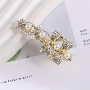 Detailed view of gold-tone metal rhinestone and pearl bow hair clip, elegant hair accessory.