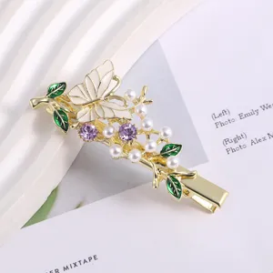 Gold metal hair clip featuring a white enamel butterfly, green leaves, pearls, and purple rhinestones.