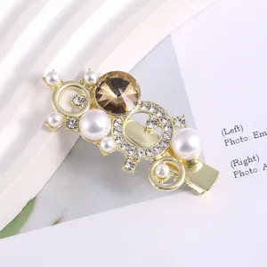 Gold tone metal hair clip featuring faux pearls, rhinestones and a brown central crystal.