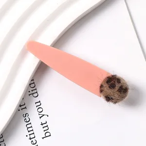 Detail shot of a cute pink resin duckbill hair clip decorated with a chic leopard print pom-pom.