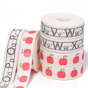Detailed shot of cotton ribbon roll with alphabet letters and red apple print for gift wrapping.